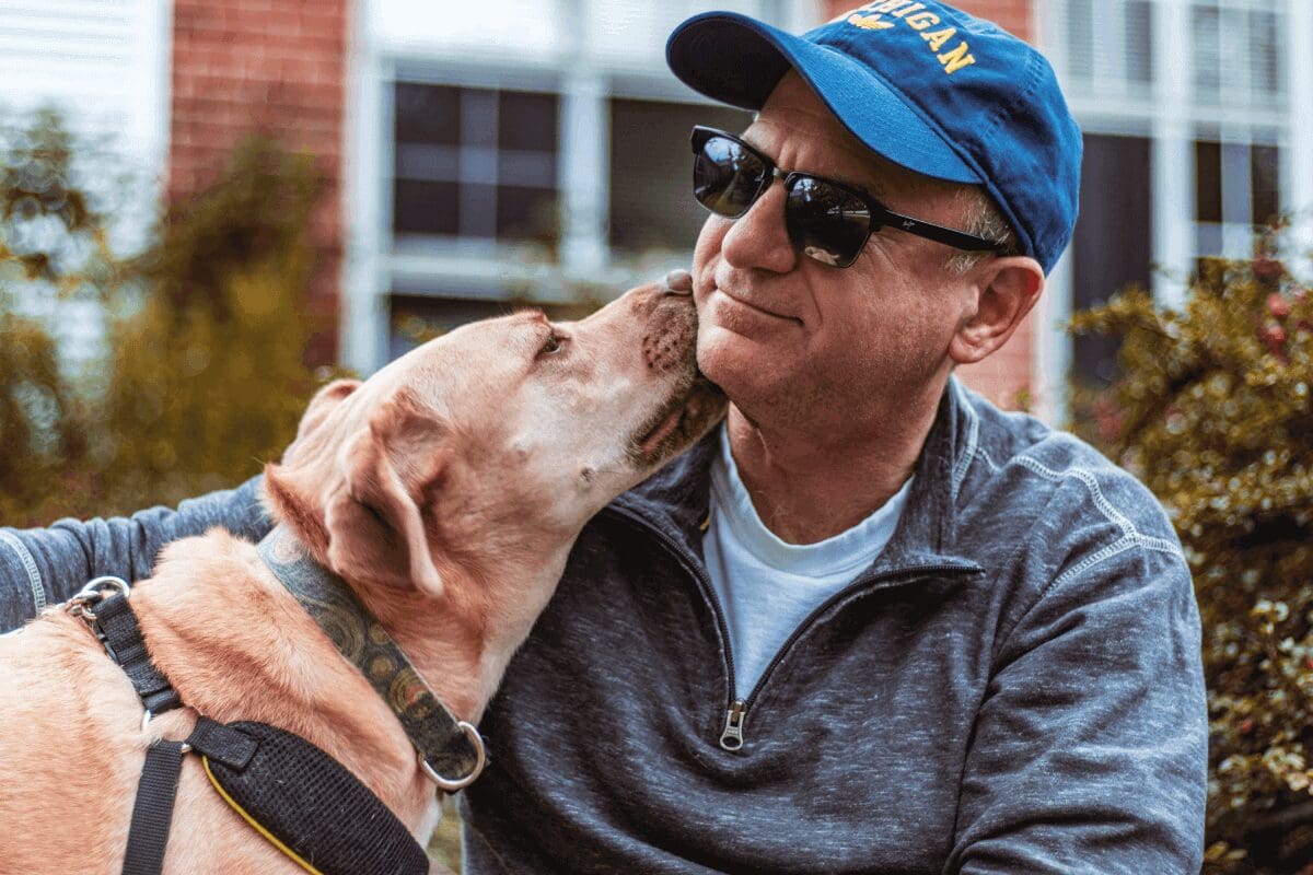 A man and his dog are kissing each other.
