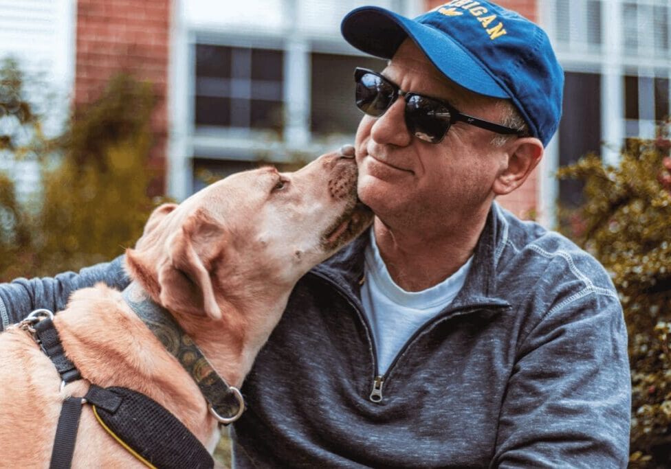 A man and his dog are kissing each other.